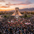 Crowd holding Iranian flags in front of Azadi Tower at sunset